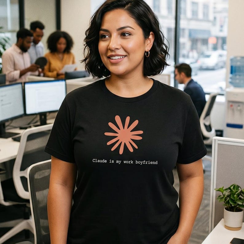 May include: A black t-shirt with a coral-colored floral design and the text "Claude is my work boyfriend." The shirt is being worn in an office setting.