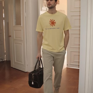 May include: A person wearing a yellow t-shirt with a red floral design and the text "You're absolutely right -" paired with khaki pants and tan shoes. They are carrying a black duffel bag.