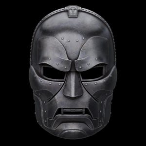 May include: A metallic gray full-face mask featuring a textured, riveted surface design. The mask includes rectangular eye openings, a prominent nose bridge, and a structured jawline with a horizontal mouth vent, all finished in a dark steel tone.