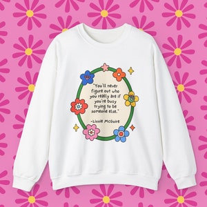 Op de afbeelding: Witte trui met een groene cirkel en kleurrijke bloemen eromheen. De tekst in de cirkel luidt "You'll never figure out who you really are if you're busy trying to be someone else." -Lizzie McGuire