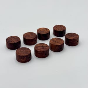 Może przedstawiać: Osiem okrągłych drewnianych gałek w ciemnobrązowym kolorze. Gałki mają mały otwór w środku.