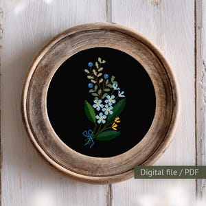 May include: A digital cross stitch pattern featuring a bouquet of blue and white flowers with green leaves and yellow accents on a black background. The pattern is framed in a wooden frame.