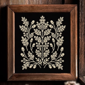 Puede incluir: Un punto de cruz enmarcado con un diseño botánico simétrico. La obra de arte muestra un patrón floral de color crema sobre un fondo negro. El marco es de madera marrón oscuro, lo que añade un toque rústico a la pieza.
