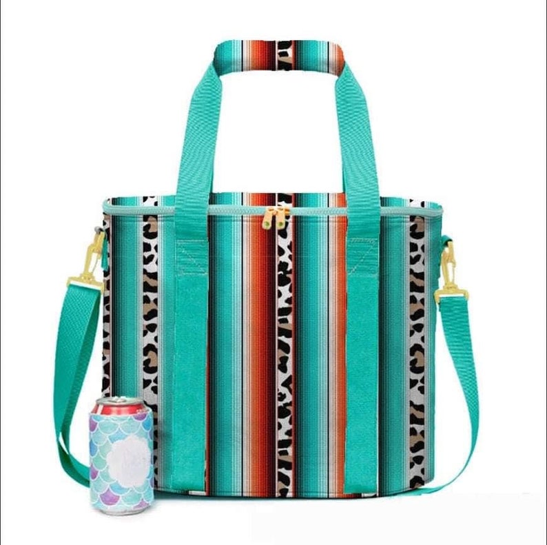 May include: A turquoise and brown striped cooler bag with a matching handle and shoulder strap. The bag features a gold zipper and a leopard print accent. A can cooler with a mermaid scale design is next to the bag.