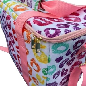 May include: A white tote bag with a colorful leopard print pattern in shades of orange, yellow, green, purple, and pink. The bag has pink straps and a pink zipper. The zipper pulls are gold.