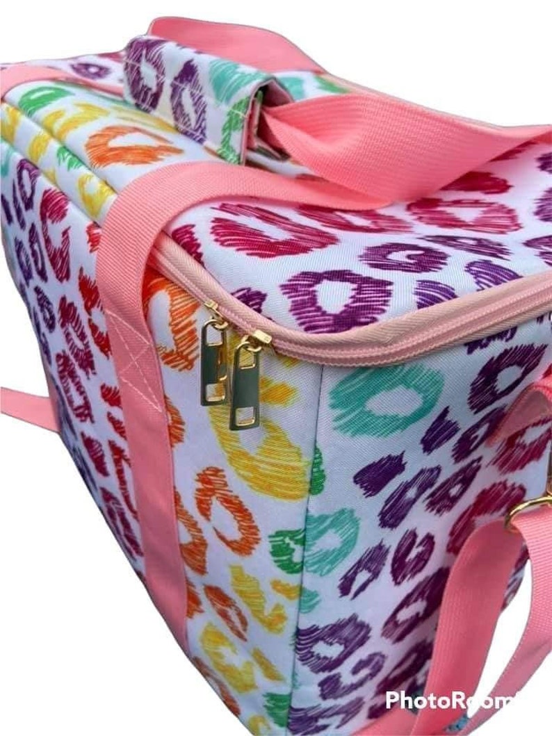May include: A white tote bag with a colorful leopard print pattern in shades of orange, yellow, green, purple, and pink. The bag has pink straps and a pink zipper. The zipper pulls are gold.