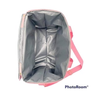 May include: Pink insulated tote bag with a silver interior. The bag has a rectangular shape with a zipper closure and pink handles. The bag is designed to keep items cold or hot.