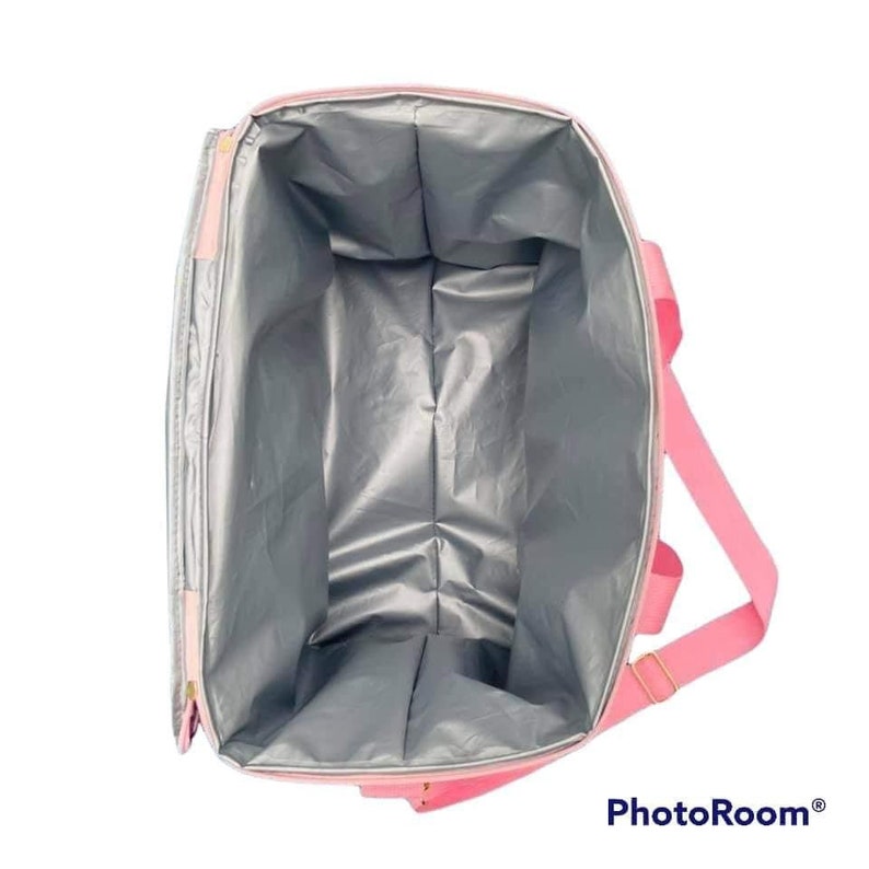 May include: Pink insulated tote bag with a silver interior. The bag has a rectangular shape with a zipper closure and pink handles. The bag is designed to keep items cold or hot.