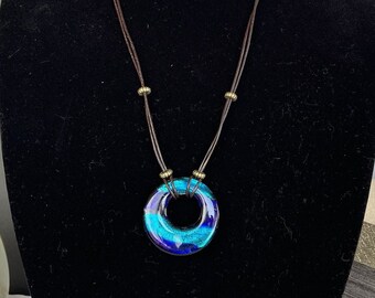 May include: A blue and purple glass circle pendant necklace with a brown leather cord and gold beads.