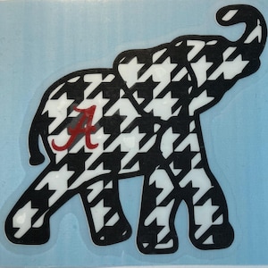 May include: Black and white houndstooth patterned elephant silhouette with a red "A" in the center.