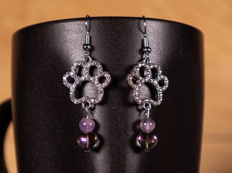 Rhinestone Paw Print Dangle Earrings with an iridescent heart bead and purple round bead.