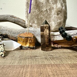May include: A collection of crystals and stones, including a clear quartz point, a tiger's eye point, a black onyx bracelet with a tiger's eye bead, and a selenite slab with a spotted stone pendant on a silver chain.