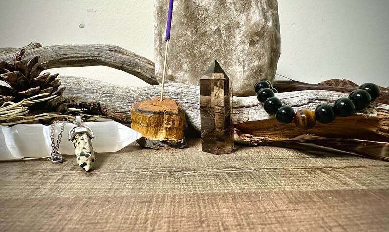 May include: A collection of crystals and stones, including a clear quartz point, a tiger's eye point, a black onyx bracelet with a tiger's eye bead, and a selenite slab with a spotted stone pendant on a silver chain.