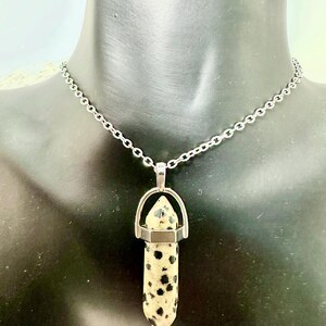 May include: A silver chain necklace with a dalmatian jasper pendant. The pendant is a point with a silver cap and a silver bail.