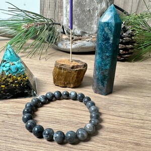 May include: A set of crystals for meditation and healing, including a turquoise pyramid, a blue-green crystal point, a black beaded bracelet, and a wooden incense holder.