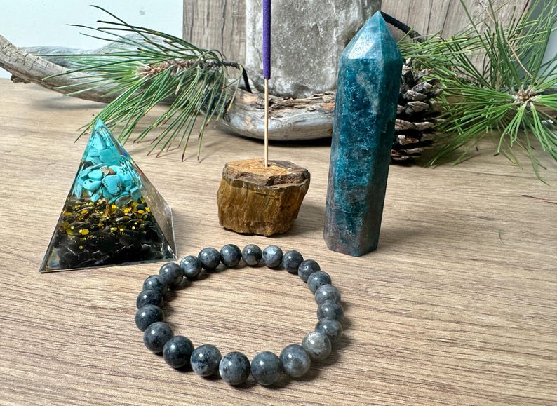 May include: A set of crystals for meditation and healing, including a turquoise pyramid, a blue-green crystal point, a black beaded bracelet, and a wooden incense holder.