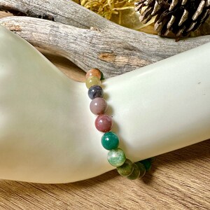 May include: A multi-colored gemstone bracelet with round beads in shades of green, pink, yellow, and blue.