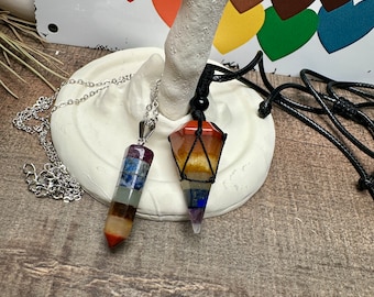 May include: Two crystal point pendants on display. One is a silver chain with a multi-colored crystal point, the other is a black cord with a multi-colored crystal point.