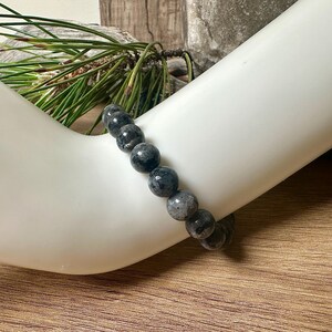 May include: A black and grey beaded bracelet made of round, smooth stones. The bracelet is worn on a person's wrist.