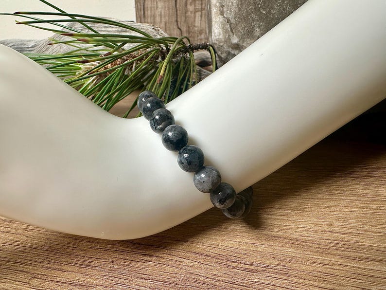 May include: A black and grey beaded bracelet made of round, smooth stones. The bracelet is worn on a person's wrist.