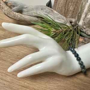 May include: A black beaded bracelet with dark grey and silver flecks. The bracelet is made of round beads and is worn on a white mannequin hand.