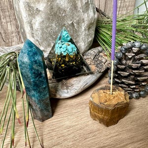 May include: A crystal pyramid with turquoise and gold accents, a blue-green crystal point, a brown and gold tiger's eye incense holder, and a purple incense stick.