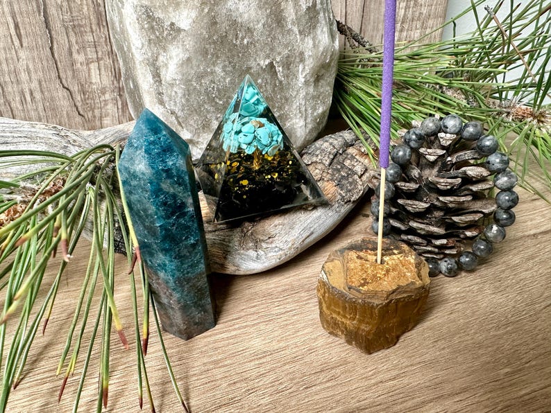May include: A crystal pyramid with turquoise and gold accents, a blue-green crystal point, a brown and gold tiger's eye incense holder, and a purple incense stick.