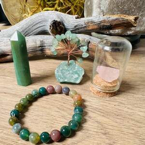 May include: A green agate crystal point, a green agate tree, a green agate bracelet, and a pink rose quartz in a glass jar with a cork lid.