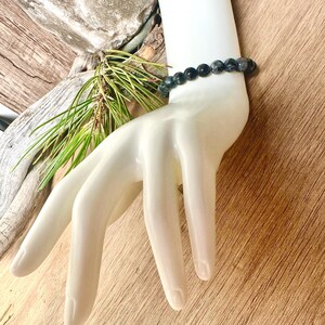 May include: A black and grey beaded bracelet on a white mannequin hand. The bracelet is made of round beads and is about 7 inches long.