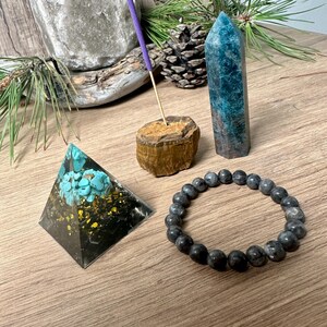 May include: A set of four crystals: a black pyramid with turquoise and gold accents, a blue-green crystal point, a brown tiger's eye crystal, and a black beaded bracelet.
