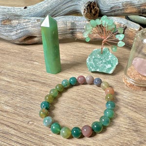 May include: A green agate crystal point, a green agate tree, a green and pink agate bracelet, and a glass jar with a pink rose quartz crystal inside.