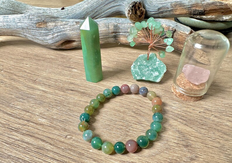 May include: A green agate crystal point, a green agate tree, a green and pink agate bracelet, and a glass jar with a pink rose quartz crystal inside.