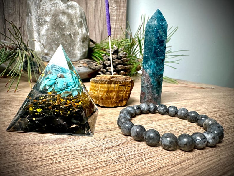 May include: A crystal pyramid with a turquoise tree inside, a blue crystal point, a brown tiger's eye stone, and a grey beaded bracelet.