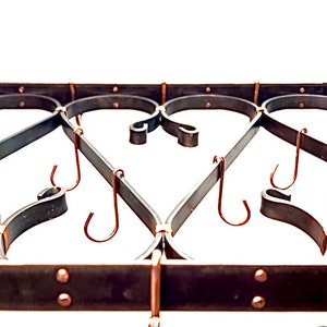 May include: A black metal pot rack with decorative scrollwork and multiple hooks. The hooks are made of copper and are hanging down from the rack.