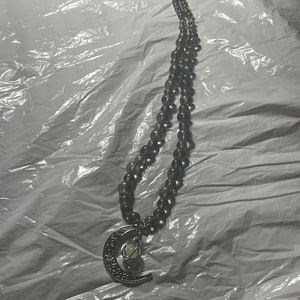 May include: A silver necklace with a crescent moon pendant and a small orb in the center. The necklace is made of dark gray beads.