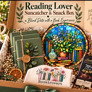 May include: A gift box labeled Reading Lover Suncatcher & Snack Box containing three green books with wax seals, a circular stained glass suncatcher with a floral and book design, a white shirt with a floral book graphic, and a Lindt dark chocolate bar.