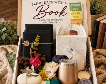 May include: A gift box labeled Blind Date with a Book containing black wrapped items with gold wax seals, a white box with floral patterns, Stash tea bags, a rose gold tumbler, a white soap bar with a key charm, and a small candle in a tin.