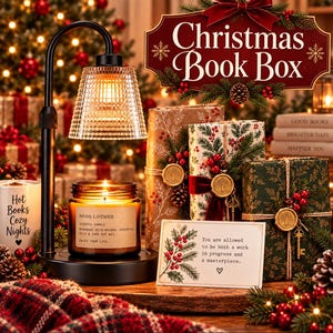 May include: A black candle warmer lamp with a textured glass shade illuminating a jar candle labeled No.03 Lavender. Beside it are three wrapped books, a card with the text You are allowed to be both a work in progress and a masterpiece, and a mug.