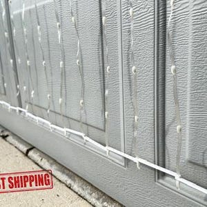 May include: White LED Christmas lights strung in a net pattern on a gray garage door. The lights are connected to a white wire running along the bottom of the door. The text "MADE IN USA" and "FAST SHIPPING" is visible in the lower left corner of the image.
