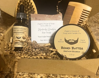 May include: A gift box filled with beard care products, including beard oil, beard butter, a bar of soap, a wooden comb, and a brush. The products are all from Ziggie's House of Soap and Candle Co. and feature the scent Kentucky Bourbon.