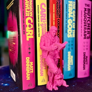 May include: A collection of colorful books from the "Dungeon Crawler Carl" series, with a pink figurine of a man reading. The book spines are pink, yellow, red, blue, and pink, with titles and author names in white and yellow.