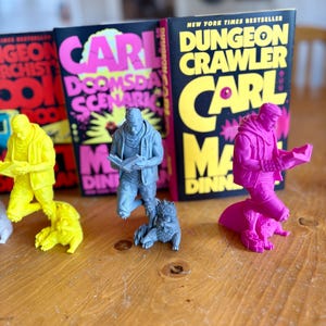 May include: A collection of colorful figurines and books. The figurines are in yellow, gray, and pink, each depicting a person reading. The books have black covers with bright text, including "CARL" and "DUNGEON CRAWLER".