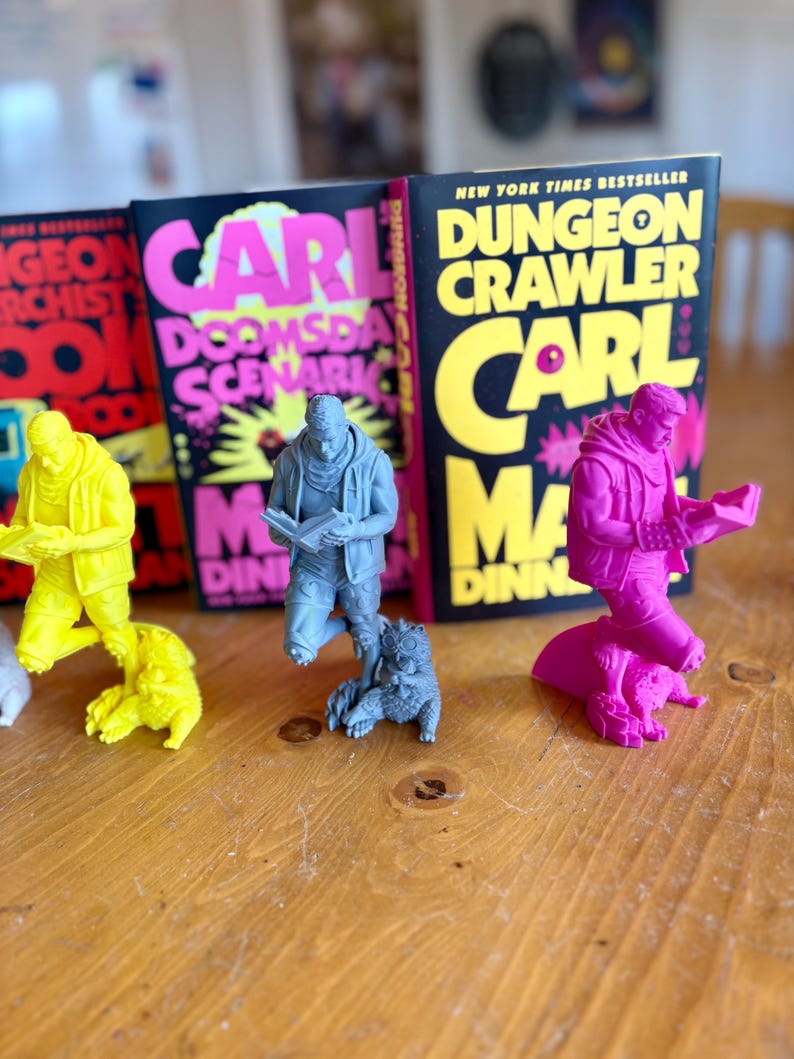 May include: A collection of colorful figurines and books. The figurines are in yellow, gray, and pink, each depicting a person reading. The books have black covers with bright text, including "CARL" and "DUNGEON CRAWLER".