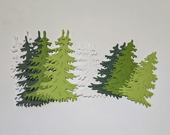 May include: A collection of flat, die-cut paper pine tree shapes in varying shades of light green, dark green, and white. The trees feature detailed, jagged branch silhouettes and are arranged in a layered, overlapping horizontal cluster.