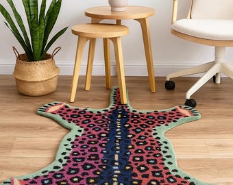 May include: A colorful rug shaped like a jaguar, featuring a green border and a pattern of pink, black, and blue spots. The rug has a detailed jaguar face design at one end, adding a playful touch to home decor.