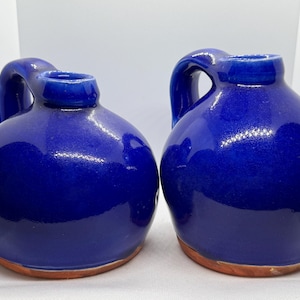 May include: Two blue ceramic jugs with a rounded body and a handle. The jugs have a brown rim.