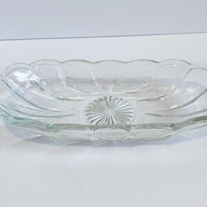 May include: Clear glass serving dish with a scalloped rim and a starburst design in the center. The oval-shaped dish is made of clear glass and is likely used for serving appetizers or small dishes.