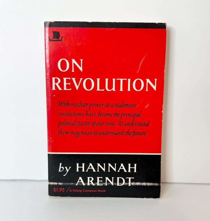 May include: A paperback book titled On Revolution by Hannah Arendt. The cover is bright red with a black horizontal band at the bottom. The text reads: On Revolution, With nuclear power at a stalemate, revolutions have become the principal political factor of our time. To understand them may mean to understand the future, by Hannah Arendt, $1.95 / A Viking Compass Book.