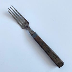 May include: An antique fork with a wooden handle. The metal tines show signs of age and wear. The handle is a dark brown color with small green accents. The fork is a vintage kitchen utensil.