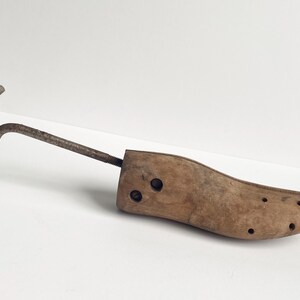 May include: A vintage wooden shoe stretcher with a metal handle and screw mechanism. The wooden form is light brown with several small holes along the toe. The metal components show signs of age.